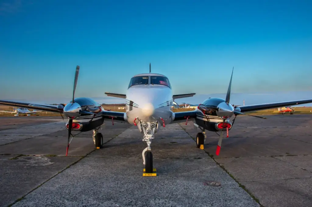 A front view of a twin-engine aircraft on tarmac under clear blue skies