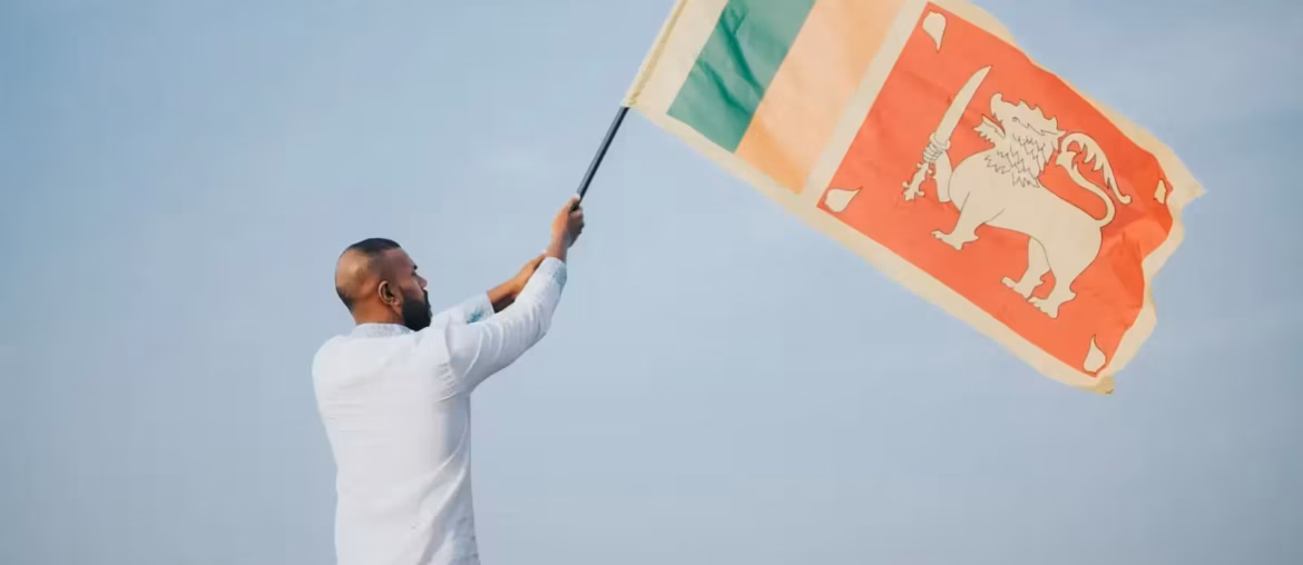 A man proudly waves the Sri Lankan flag outdoors under a clear blue sky, symbolizing national pride