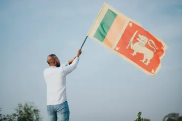 A man proudly waves the Sri Lankan flag outdoors under a clear blue sky, symbolizing national pride