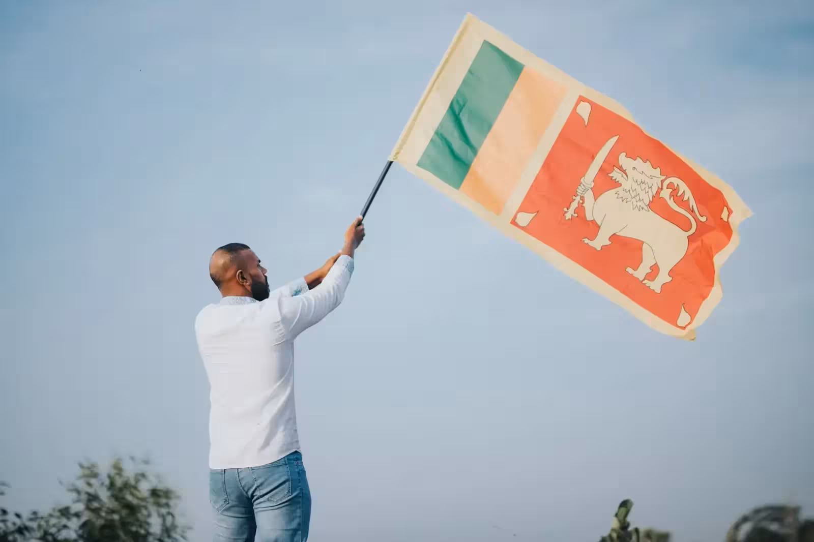 Can You Rent a Garba Partner? Why Cops Stepped In A man proudly waves the Sri Lankan flag outdoors under a clear blue sky, symbolizing national pride