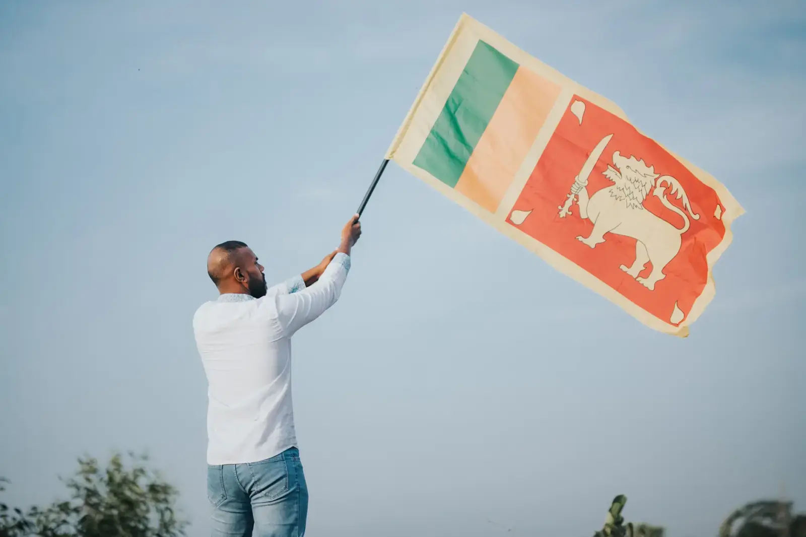 Can You Rent a Garba Partner? Why Cops Stepped In A man proudly waves the Sri Lankan flag outdoors under a clear blue sky, symbolizing national pride