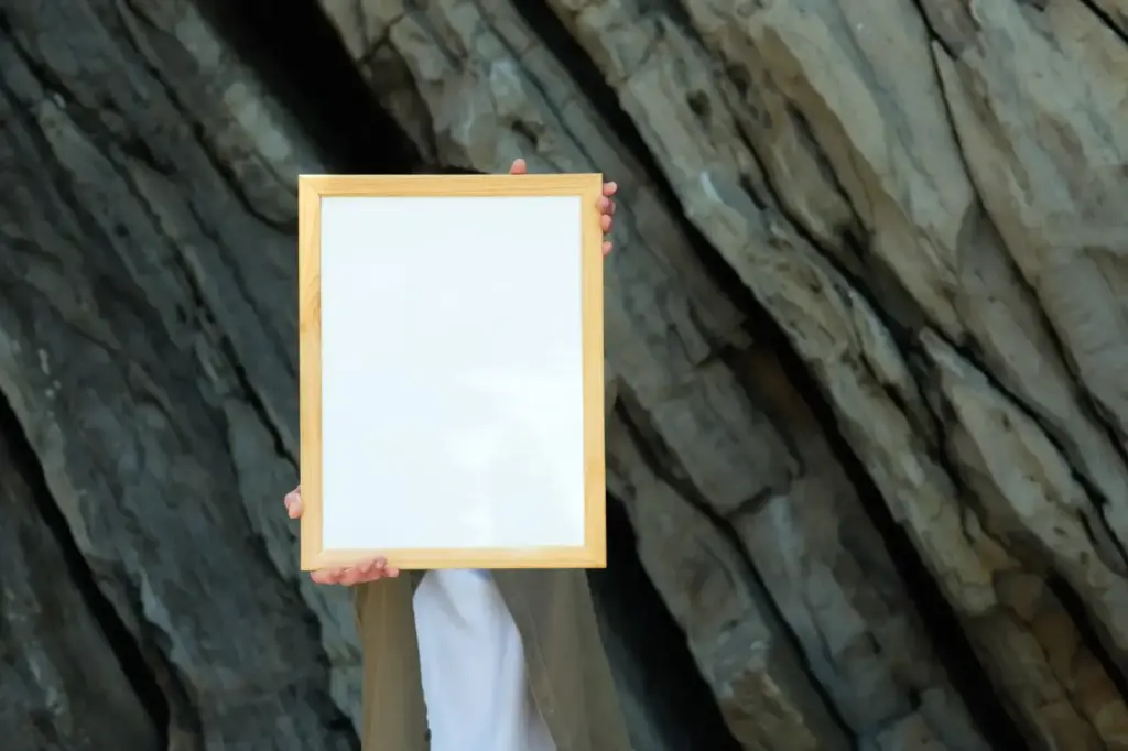 A person extends a blank wooden frame in front of rocky cliffs, ideal for mockup uses