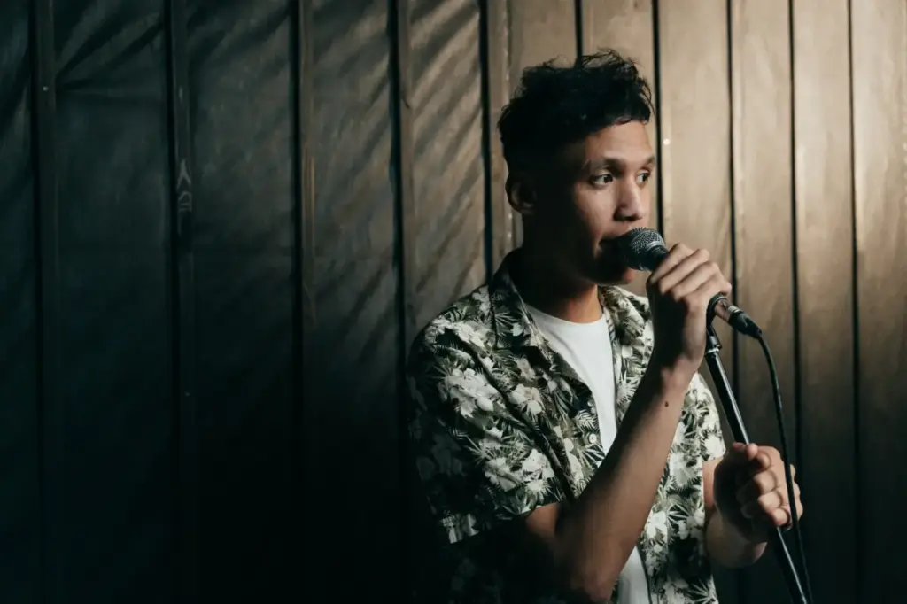 A young male singer in a floral shirt performing indoors with a microphone