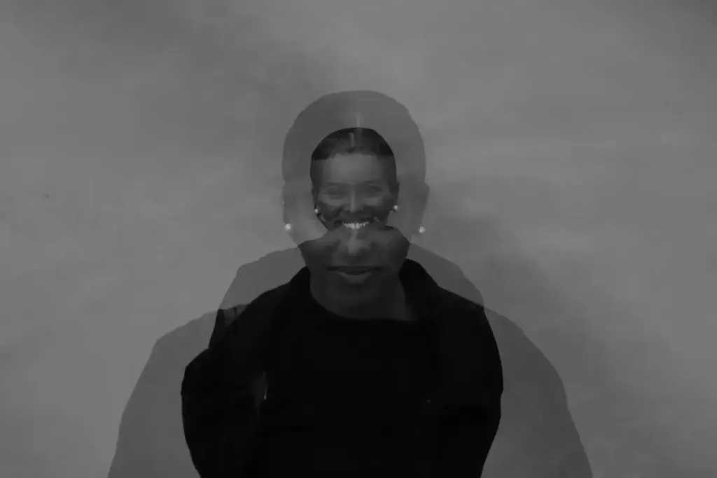 Artistic black and white double exposure portrait of a smiling woman, creating a blurred and surreal effect