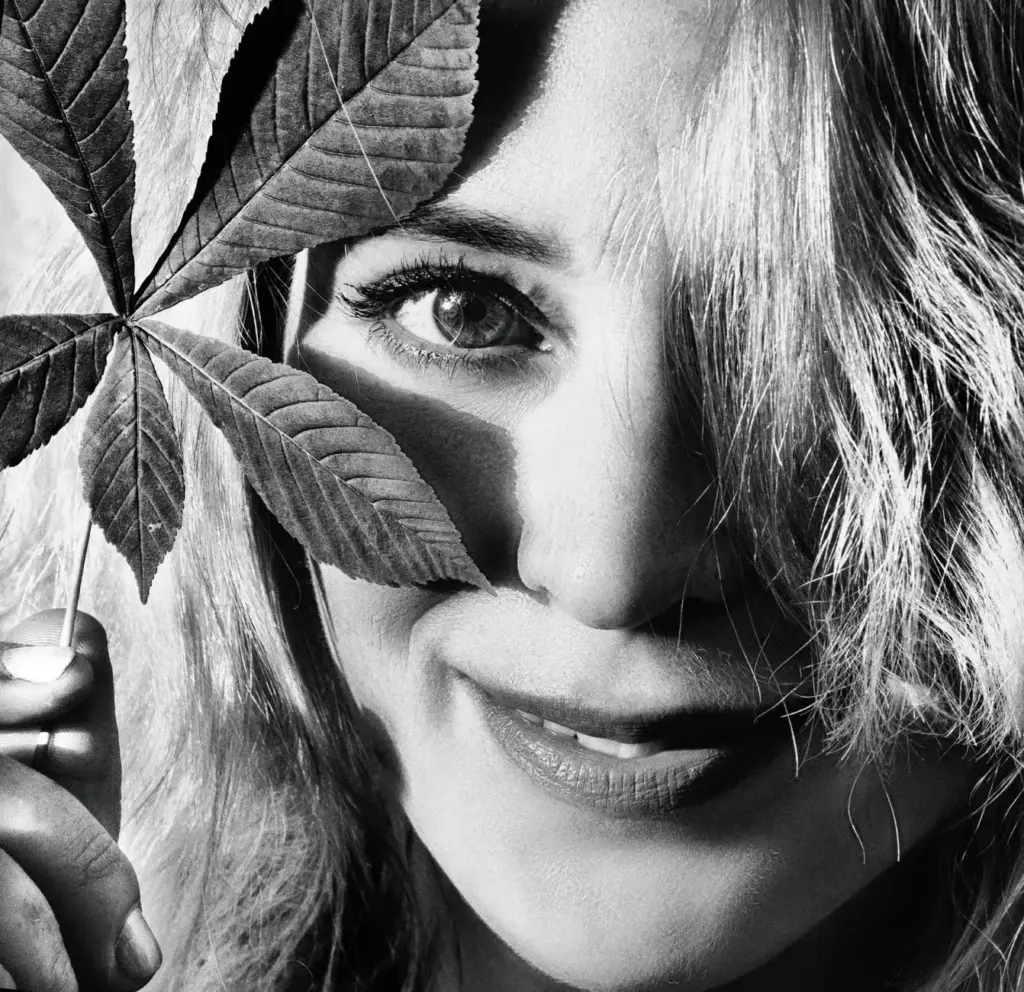 Black and white portrait of a woman smiling with a leaf held to her face, exuding elegance