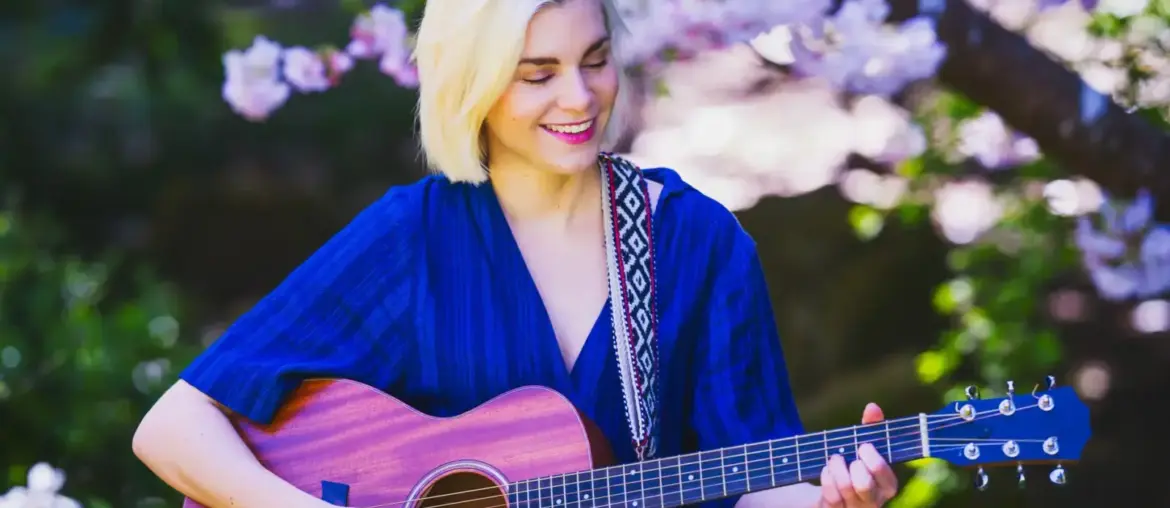 Blonde woman playing an acoustic guitar while sitting outdoors among blooming spring flowers