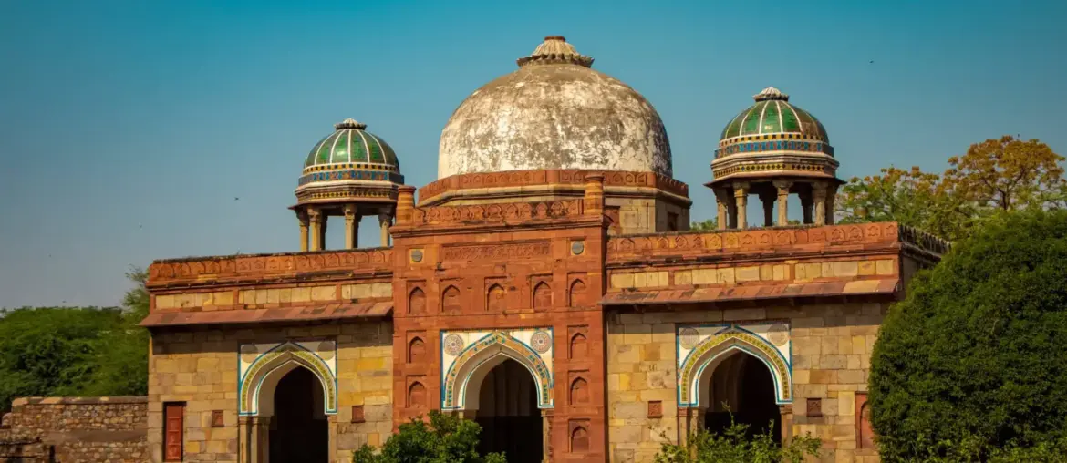Historic red sandstone dome and arched facade of Isa Khan's Tomb under a blue sky in Delhi