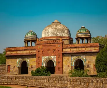 Historic red sandstone dome and arched facade of Isa Khan's Tomb under a blue sky in Delhi