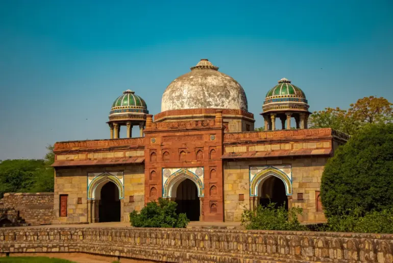 Historic red sandstone dome and arched facade of Isa Khan's Tomb under a blue sky in Delhi