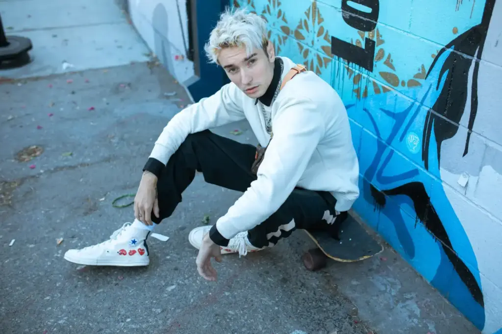 Portrait of a young man with dyed hair posing with a skateboard in an urban environment, showcasing street style
