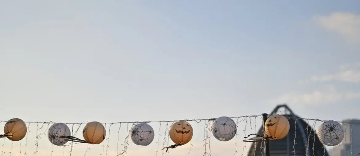String lights with Halloween lanterns hanging outdoors against a city skyline in the evening