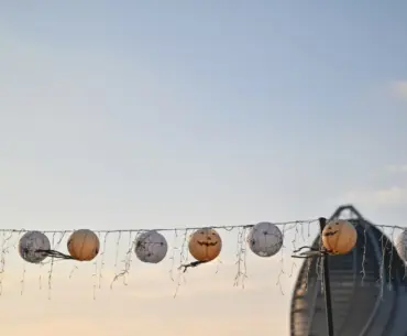String lights with Halloween lanterns hanging outdoors against a city skyline in the evening
