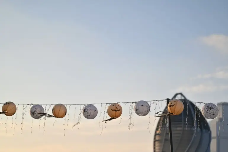 String lights with Halloween lanterns hanging outdoors against a city skyline in the evening