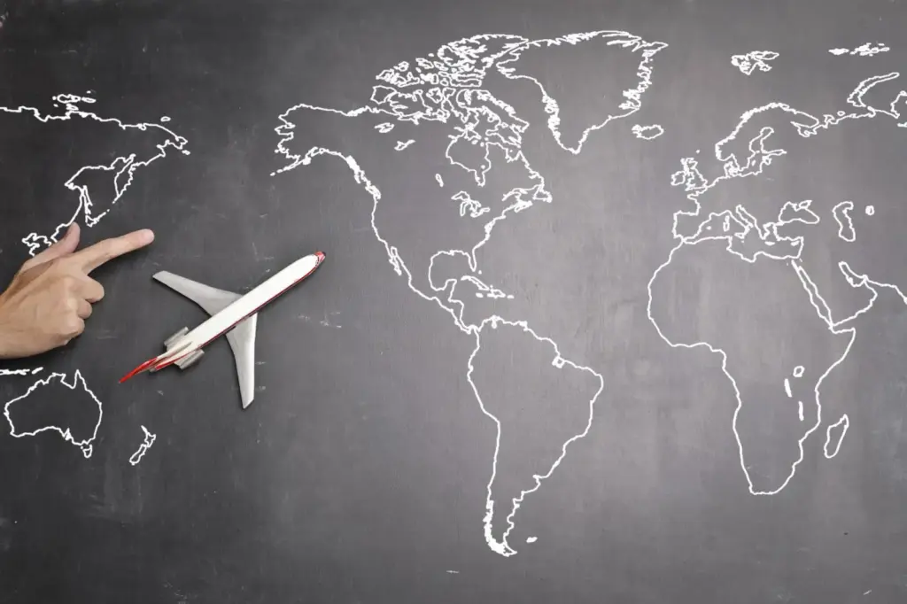 Top view of miniature airplane placed on over gray world map with crop hand of anonymous person indicating direction…