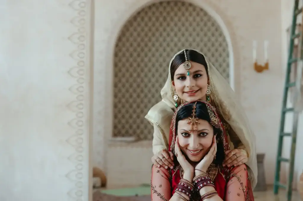 Two women in traditional Indian attire, smiling warmly indoors